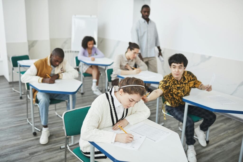 Group of students taking a test in a modern college classroom under teacher supervision because "Education is Important."